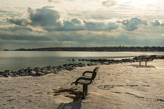 Benches in the sand in front of the rock lined water ledge in Narraganseet Bay