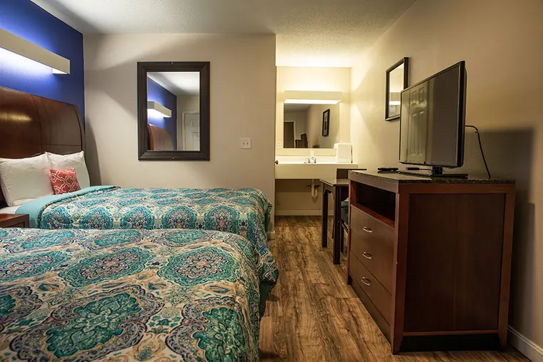 The same room showing the foot of the two beds, the dresser with the TV on top and the bathroom