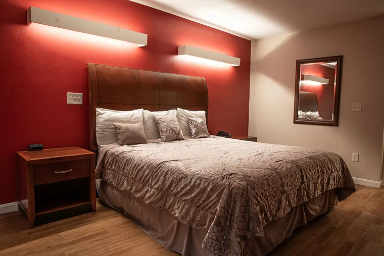Single bed with a wooden headboard against a red wall, with two overhead lights and a bedside table