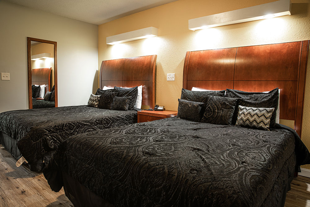2 Queen sized beds with a black paisley comforter with tall wooden headboards.