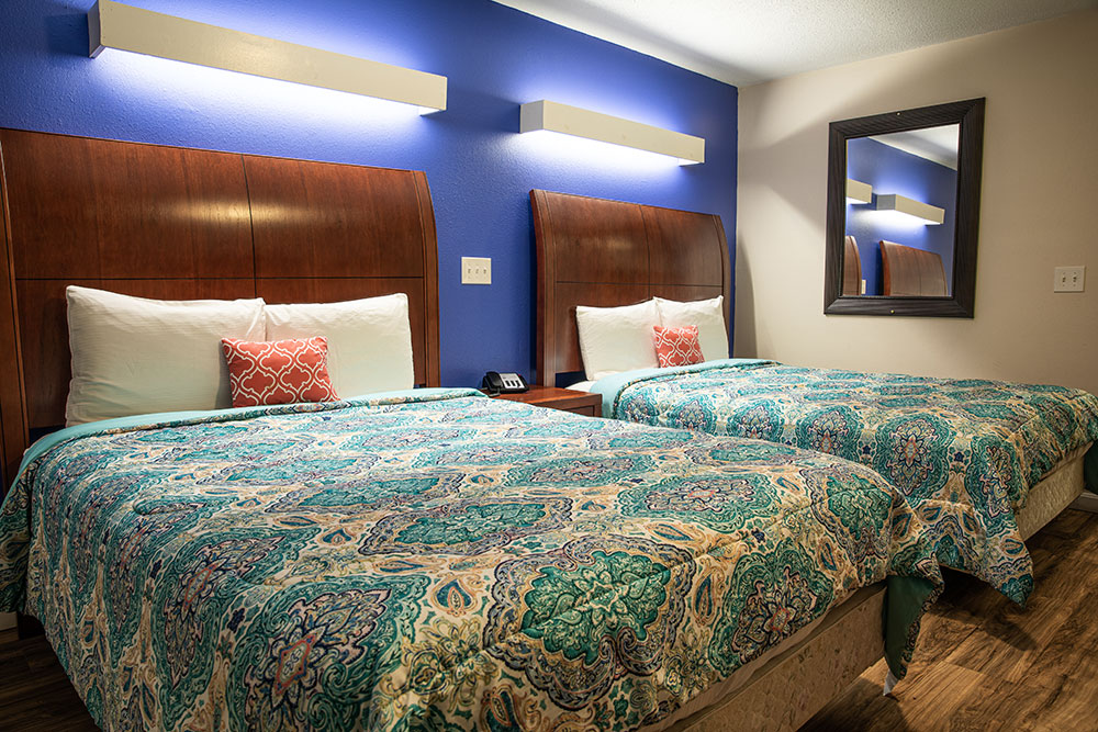 2 beds with tall wooden headboards, teal and cream paisley comforters against a royal blue wall.
