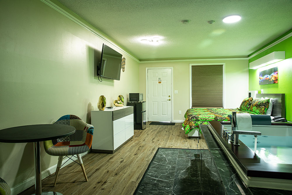 Looking towards the opposite side of the room in the jacuzzi room with the tv, fridge, microwave, dresser and 2 patchwork modern chairs and table.