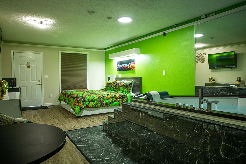 A view of the jacuzzi room from the bathroom. The jacuzzi is on the right and the bed is by the window with a green wall behind the bed