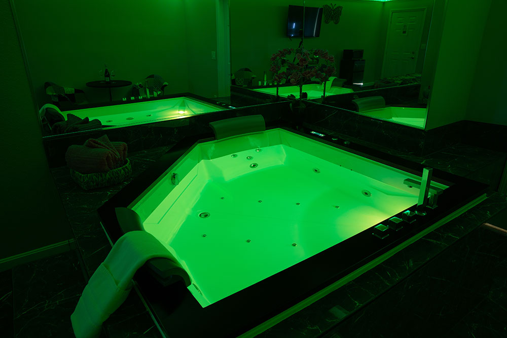 A closeup of the jacuzzi surrounded by mirrors with the lights in the jacuzzin shining green